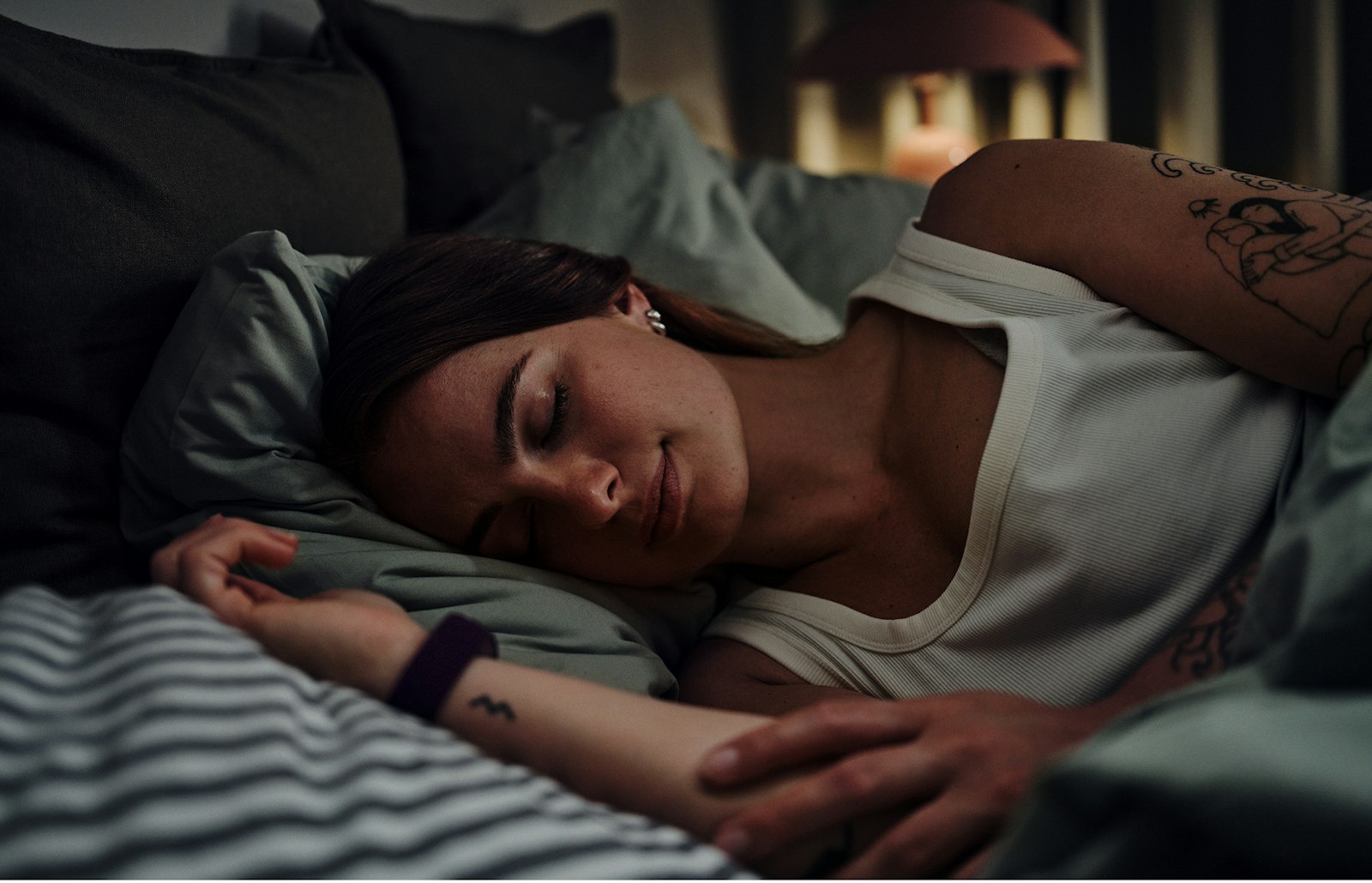 A woman asleep in bed wearing a temperature-tracking band on her wrist